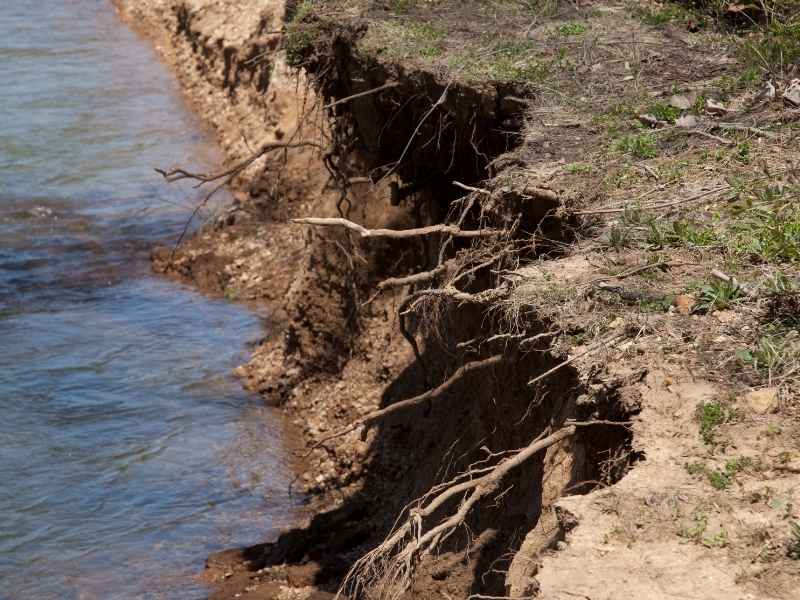 Land surveying after a washout in Bryan, Texas, showing severe erosion along a creek bank and damaged ground conditions.
