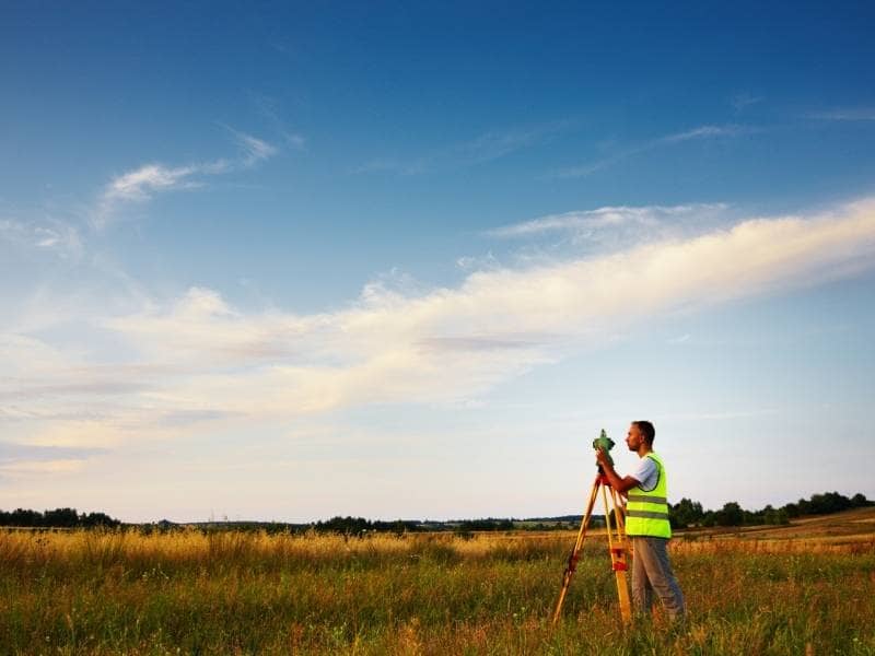 Land surveyor measuring rural property in Bryan TX to verify boundaries described by a century old deed.